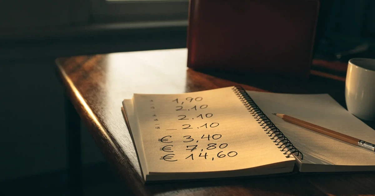 Um caderno aberto com cotas escritas à mão, uma calculadora e um lápis sobre uma mesa de madeira