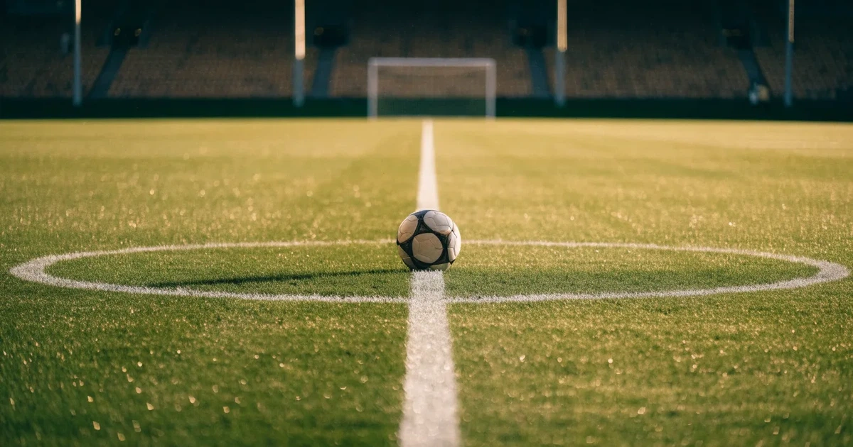 Uma bola de futebol no ponto central de um relvado, à luz da manhã